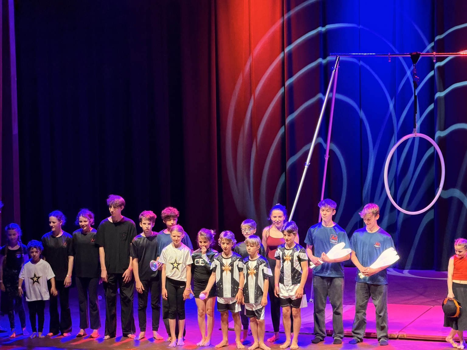 Young circus artists together on stage with juggling props and an aerial hoop